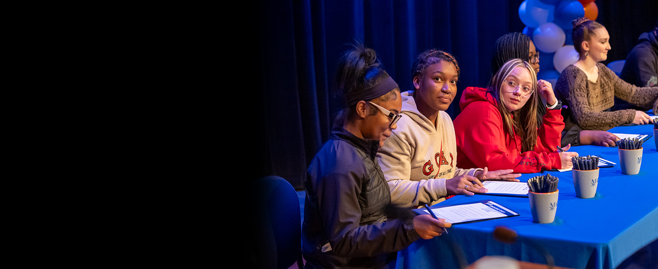 Four students signing papers at table